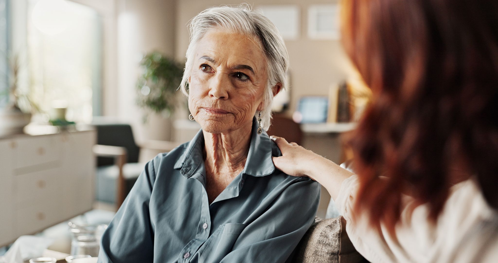 Senior woman who looks worried sits with an elder advocate ombudsman, who has her hand on the senior's shoulder in support.
